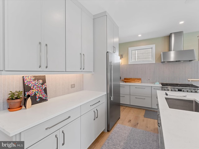 kitchen featuring wall chimney range hood, tasteful backsplash, light wood-type flooring, high end refrigerator, and light countertops