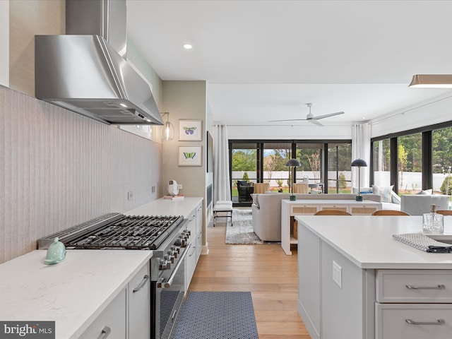 kitchen with exhaust hood, a ceiling fan, stainless steel stove, light wood finished floors, and open floor plan