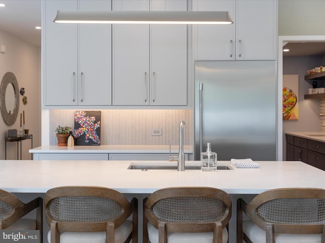 kitchen featuring a breakfast bar area, recessed lighting, light countertops, stainless steel built in fridge, and a sink