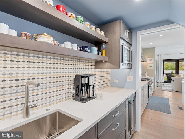 kitchen with appliances with stainless steel finishes, a sink, light wood finished floors, recessed lighting, and decorative backsplash