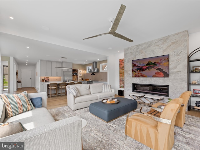 living area with recessed lighting, ceiling fan, light wood-type flooring, and a premium fireplace
