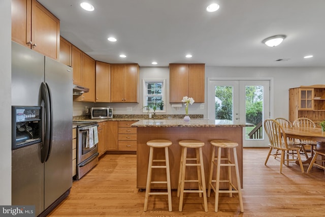 kitchen with a center island, stainless steel appliances, light wood finished floors, and under cabinet range hood
