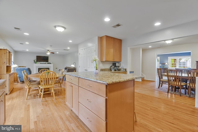 kitchen featuring ceiling fan, visible vents, light wood finished floors, and light stone countertops