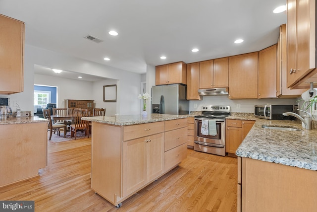 kitchen with appliances with stainless steel finishes, a sink, a center island, under cabinet range hood, and visible vents