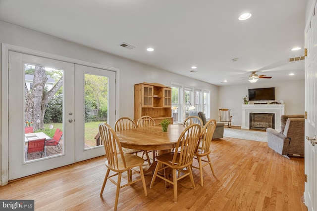 dining area featuring a glass covered fireplace, light wood-style floors, french doors, and visible vents