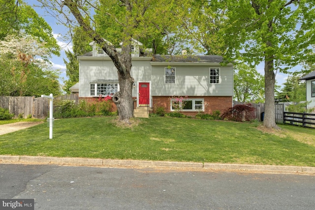 split level home featuring brick siding, a front lawn, and fence