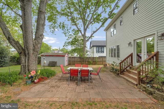 view of patio / terrace with french doors, an outbuilding, fence, a shed, and outdoor dining space