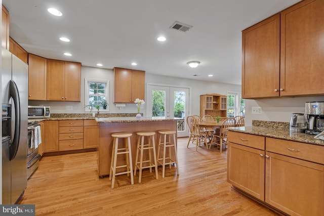 kitchen featuring light stone countertops, a breakfast bar, light wood finished floors, stainless steel appliances, and visible vents