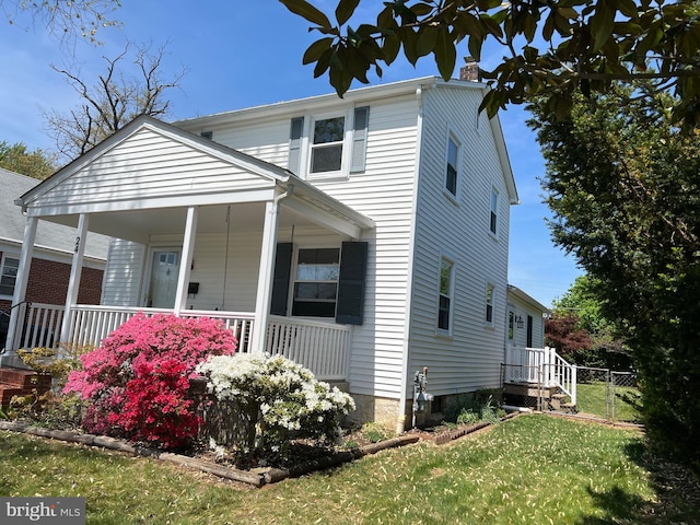 view of front facade featuring fence, a chimney, a porch, and a front lawn