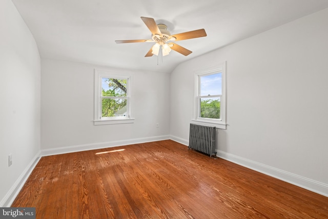 spare room with wood finished floors, baseboards, ceiling fan, and radiator heating unit