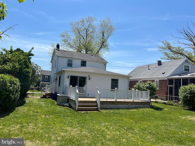 rear view of house featuring a yard, a deck, a chimney, and a sunroom