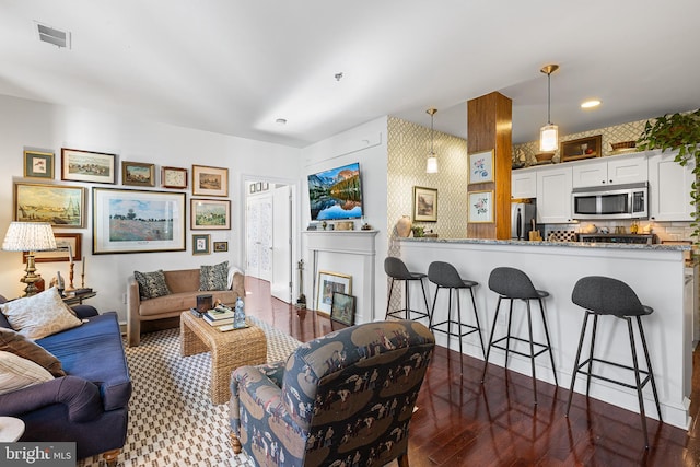 living room with visible vents, a glass covered fireplace, dark wood-type flooring, and wallpapered walls