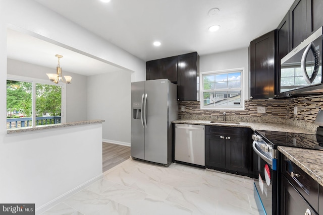 kitchen featuring appliances with stainless steel finishes, a sink, decorative backsplash, a chandelier, and light stone counters