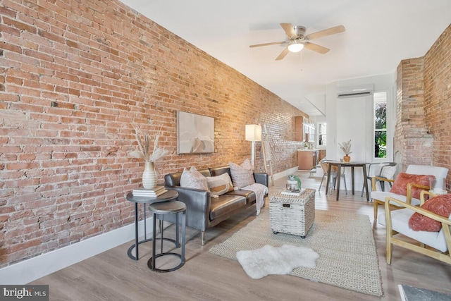 living area with baseboards, wood finished floors, and brick wall