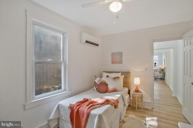 bedroom featuring an AC wall unit, baseboards, ceiling fan, and light wood-style floors