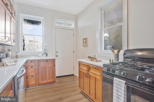 kitchen with stainless steel dishwasher, brown cabinetry, light countertops, light wood finished floors, and gas stove