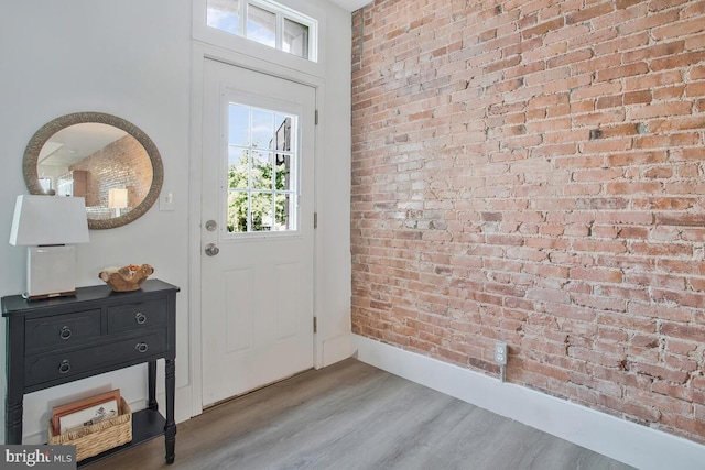 entryway with baseboards, brick wall, and light wood-type flooring