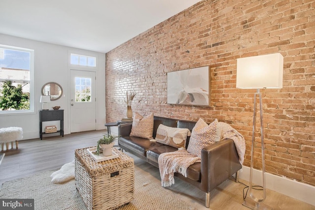 living area with baseboards, wood finished floors, and brick wall