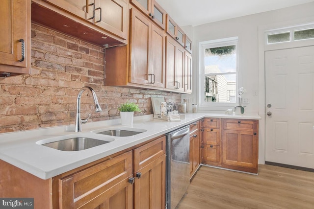 kitchen featuring stainless steel dishwasher, brown cabinets, a sink, light wood finished floors, and glass insert cabinets