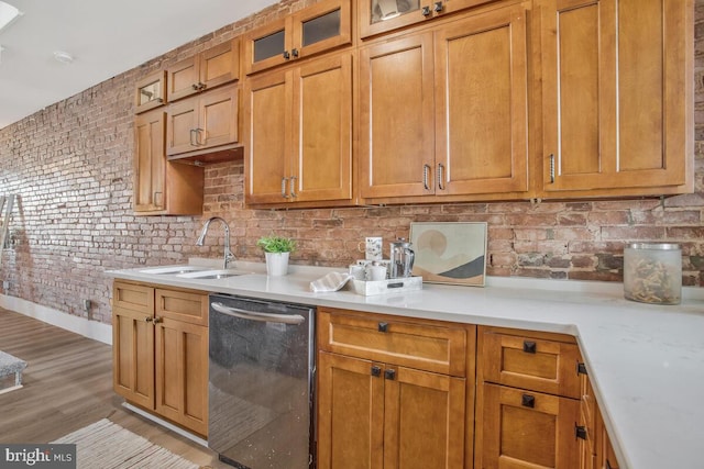 kitchen featuring brown cabinets, a sink, light wood finished floors, dishwasher, and light countertops