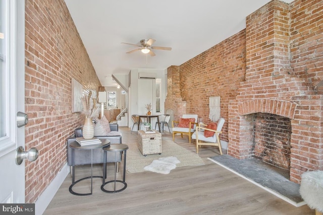 living room featuring stairway, a ceiling fan, brick wall, and wood finished floors