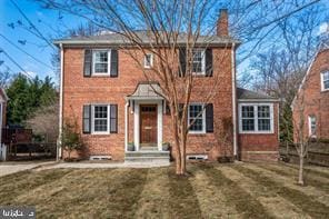 view of front of house featuring brick siding, a front lawn, and a chimney