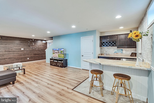 living area featuring bar with sink, wooden walls, recessed lighting, light wood-style floors, and baseboards