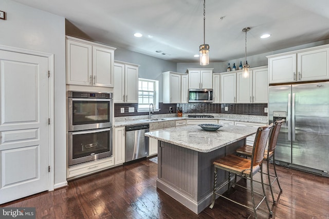 kitchen featuring appliances with stainless steel finishes, a sink, a kitchen bar, decorative backsplash, and a kitchen island
