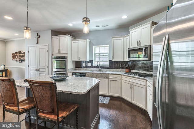 kitchen featuring appliances with stainless steel finishes, a sink, backsplash, pendant lighting, and white cabinets
