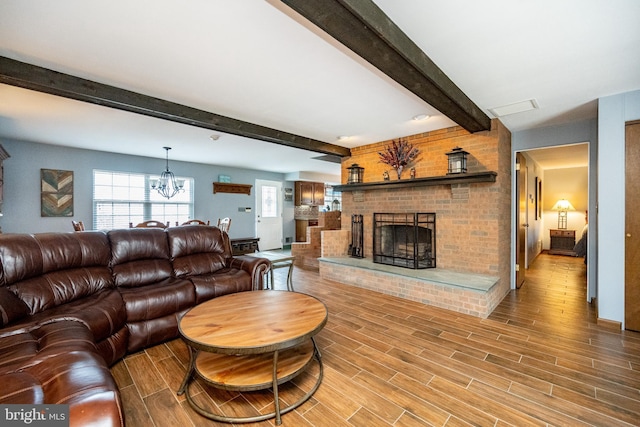 living room with wood finished floors, a fireplace, beamed ceiling, and a notable chandelier