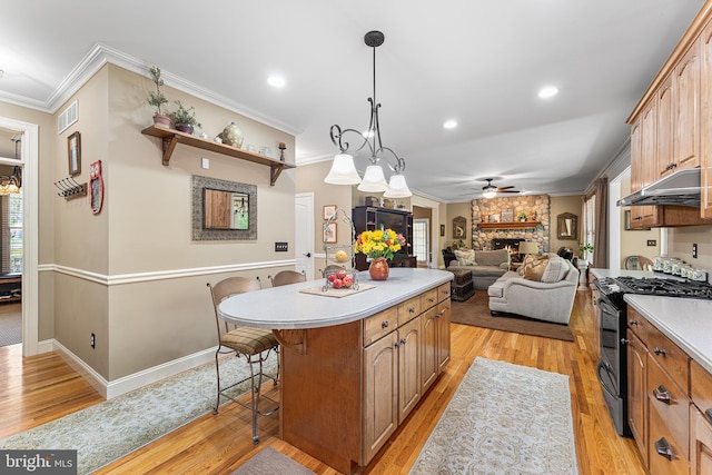 kitchen featuring gas stove, under cabinet range hood, a breakfast bar area, light countertops, and a stone fireplace
