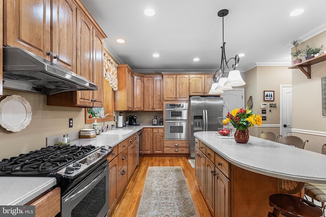 kitchen featuring appliances with stainless steel finishes, under cabinet range hood, a sink, crown molding, and light wood finished floors