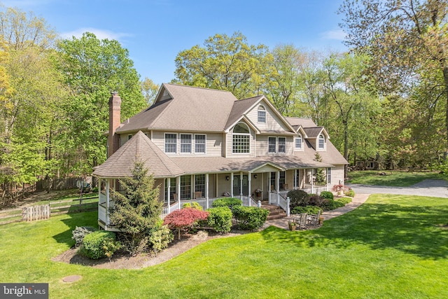 view of front of house featuring covered porch, a front lawn, a chimney, and a shingled roof
