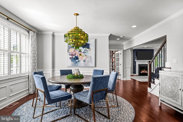 dining space featuring wood finished floors, ornamental molding, a warm lit fireplace, recessed lighting, and wainscoting