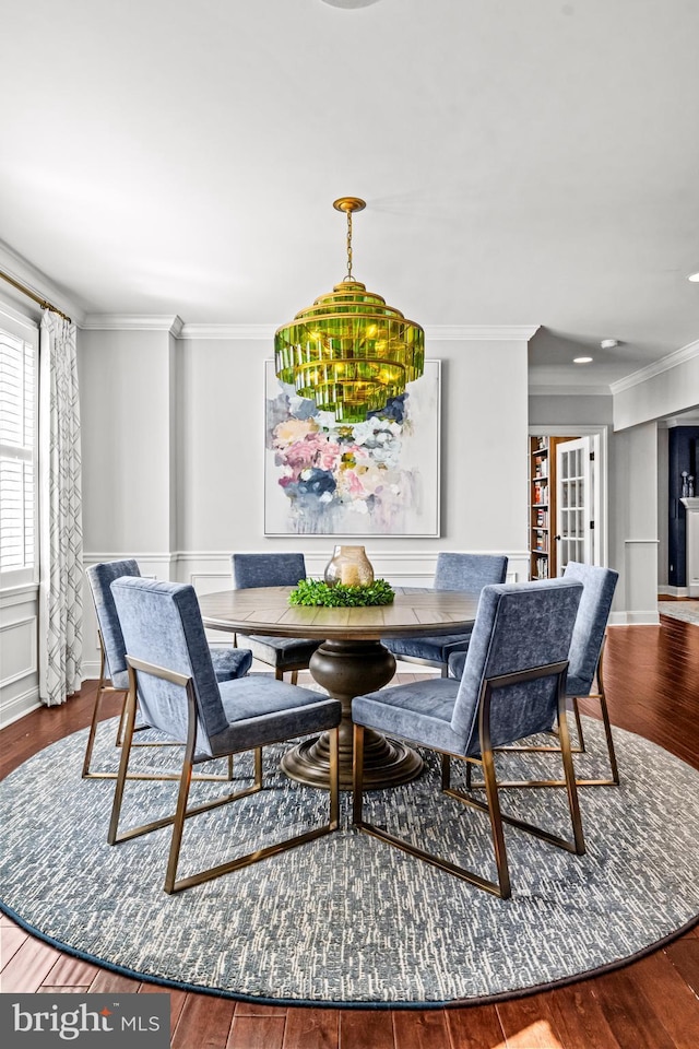 dining room featuring wood finished floors, ornamental molding, and wainscoting