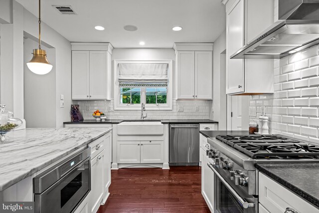 kitchen with appliances with stainless steel finishes, a sink, wall chimney exhaust hood, white cabinetry, and recessed lighting