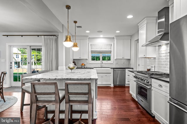 kitchen with stainless steel appliances, wall chimney exhaust hood, tasteful backsplash, white cabinets, and recessed lighting