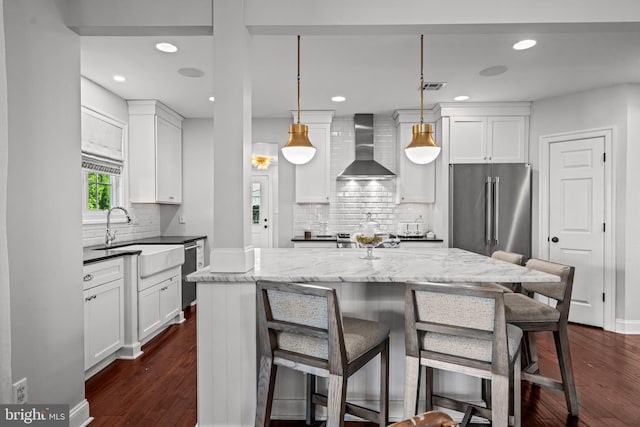 kitchen with wall chimney exhaust hood, high quality fridge, a sink, white cabinets, and dishwashing machine