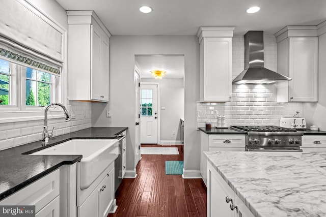 kitchen with wall chimney range hood, gas stove, white cabinetry, decorative backsplash, and recessed lighting