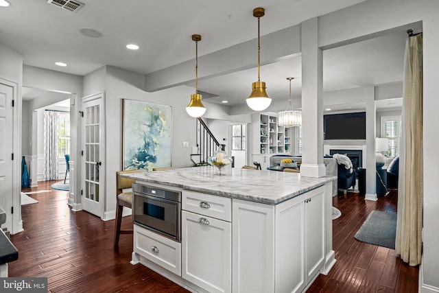 kitchen with white cabinets, dark wood-style floors, pendant lighting, light stone counters, and a fireplace