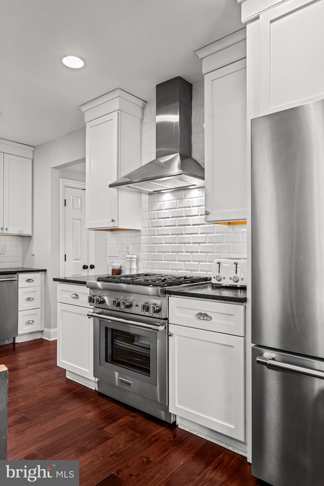 kitchen featuring stainless steel appliances, wall chimney range hood, dark countertops, backsplash, and recessed lighting