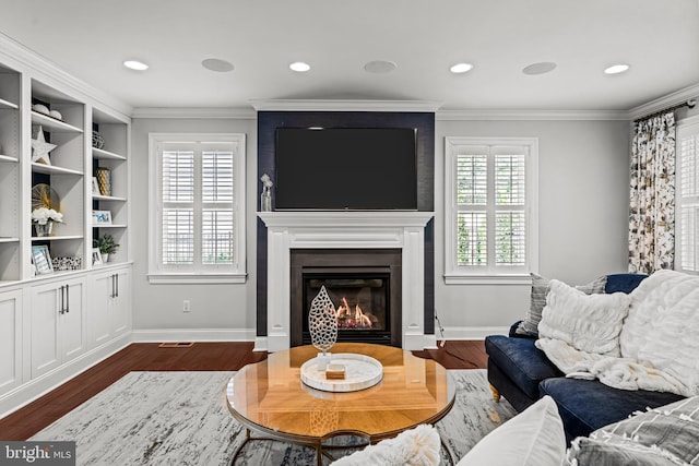 living room with a glass covered fireplace, dark wood-style floors, ornamental molding, baseboards, and recessed lighting