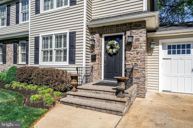 view of exterior entry featuring stone siding, an attached garage, and driveway
