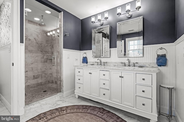 bathroom with marble finish floors, a wainscoted wall, a shower stall, and double vanity