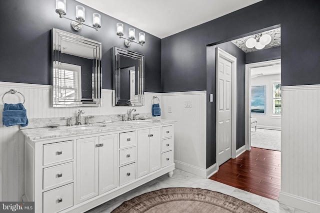 bathroom with a wainscoted wall, double vanity, plenty of natural light, and marble finish flooring