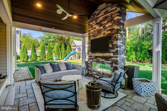 view of patio featuring an outdoor living space with a fireplace, a playground, fence, and ceiling fan