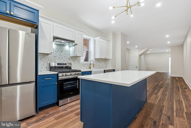1107 S Divinity St, Philadelphia, PA 19143 - kitchen featuring blue cabinets, dark wood finished floors, appliances with stainless steel finishes, backsplash, and exhaust hood