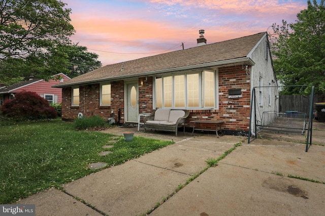 back of property with brick siding, a chimney, a lawn, and roof with shingles