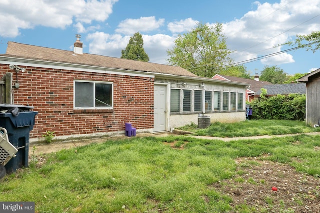 back of property with brick siding, central AC, a chimney, and roof with shingles