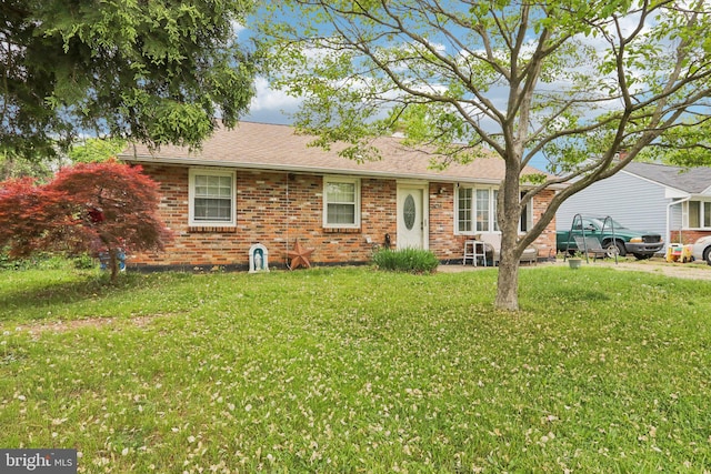 rear view of house with brick siding, a yard, and roof with shingles